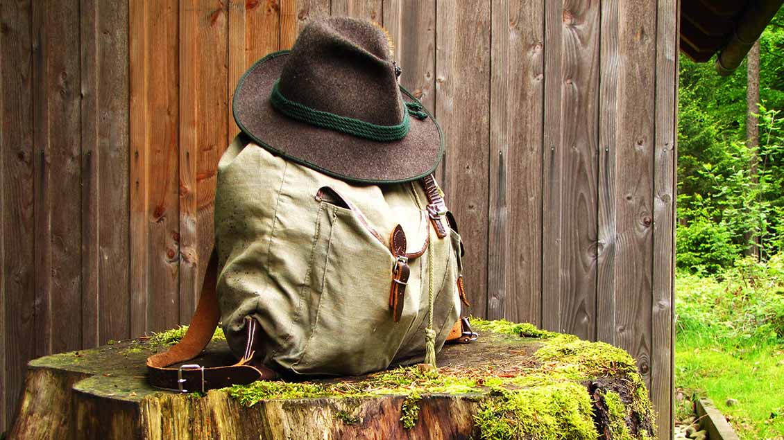 Ein Wanderrucksack mit einem Hut auf einem abgesägten Baumstamm in der Natur.
