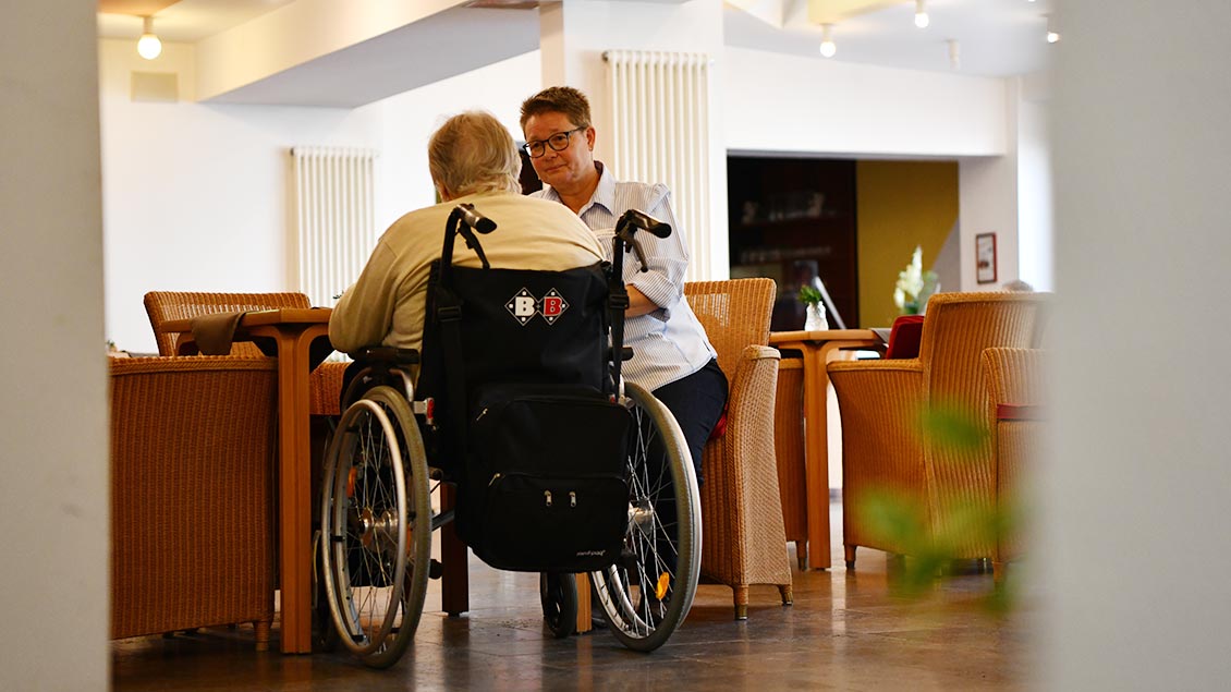 Krankenhaus-Pastoralreferentin Andrea Greshake im Gespräch mit einer Altenheimbewohnerin, die im Rollstuhl sitzt.
