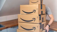 Ein Mann trägt einen Stapel Amazon-Kartons