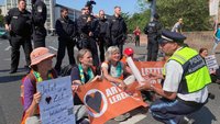 Menschen sitzen mit Bannern auf der Straße. Ein Polizist spricht mit ihnen.