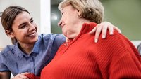 Eine Pflegekraft lächelt eine Seniorin an