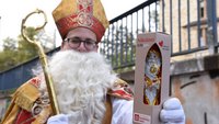 Ein Mann hat sich als Nikolaus verkleidet und hält eine Schokoladenfigur in die Kamera.