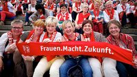 Frauen halten einen roten Schal mit dem Motto der Mitglieder-Werbekampagne "Frauen.Macht.Zukunft" hoch.