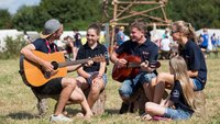 Kinder sitzen auf einer Wiese und spielen Gitarre