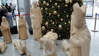 Vor einem großen Tannenbaum stehen hölzerne Figuren und eine Krippe aus Holz.