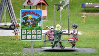 Drei Kinder sitzen auf einem Karussell.