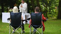 Zwei Gottesdienstteilnehmer sitzen in Klappstühlen auf der Wiese.