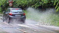 Ein Auto fährt durch eine tiefe Wasserpfütze.