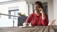 Inga Piontek telefoniert an einem Tisch auf dem Balkon.