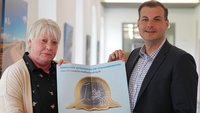 Ute Cappenberg (l.) und Dominique Hopfenzitz halten ein Plakat in die Kamera.