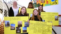 Junge Frauen und eine Lehrerin stehen auf einer Treppen und halten gelbe Plakate vor sich.