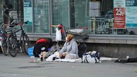 Eine Obdachlose sitzt vor einem Kaufhaus.