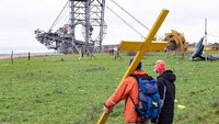 Demonstranten mit Kreuz vor Braunkohlebagger bei Lützerath