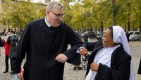 Ordensmann und Nonne begrüßen sich corona-konform auf dem Domplatz in Münster.