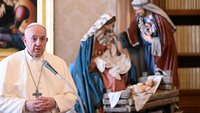 Papst Franziskus steht in der päpstlichen Bibilothek vor einer Krippe und spricht an einem Mikrofon.