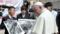 Papst Franziskus mit jungen Menschen aus Hiroshima und Nagasaki, die ihm Fotos nach den Atombombenabwürfen 1945 zeigen