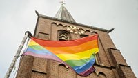 Regenbogenfahne vor einem Kirchturm