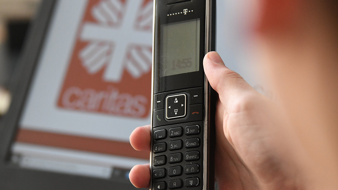 Ein Telefon mit dem Logo der Caritas im Hintergrund