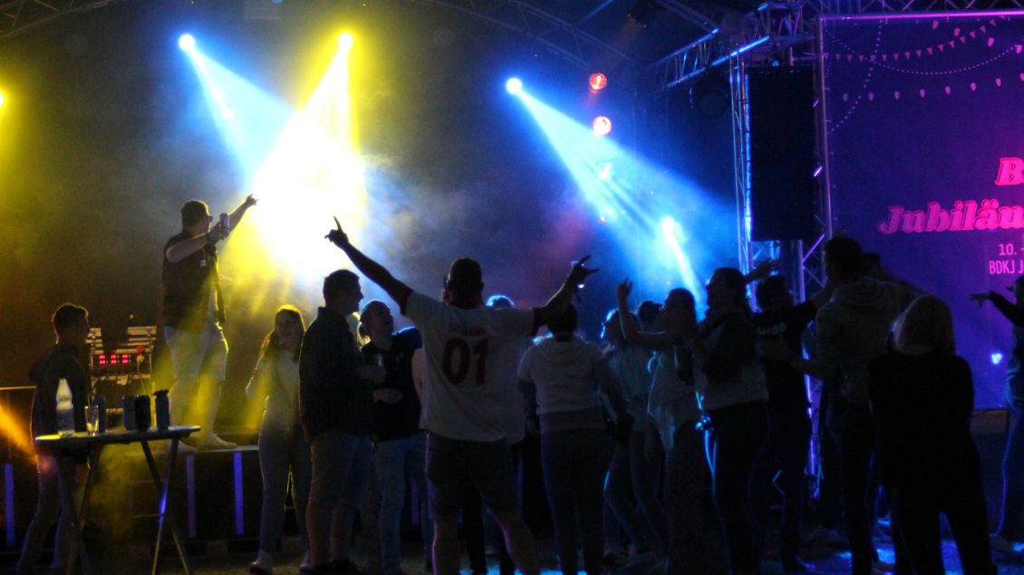 Junge Menschen feiern vor einer Bühne in buntem Licht.