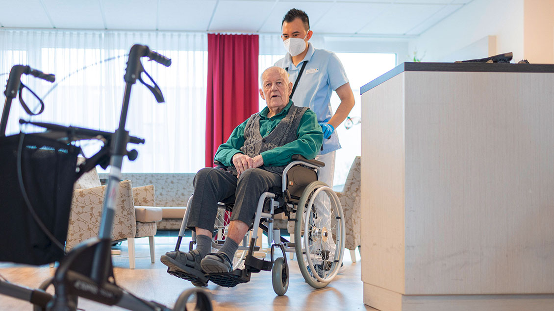 Pfleger mit Mann im Rollstuhl im Pflegeheim.