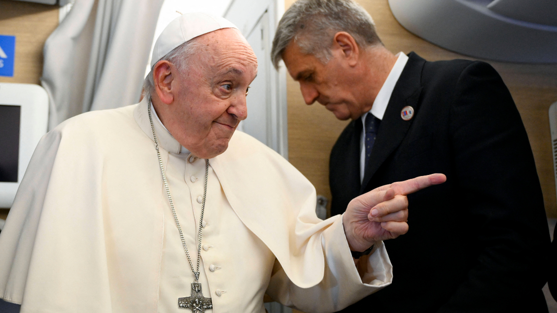 Papst steht in Flugzeugkabine und deutet mit dem Zeigefinger nach rechts.